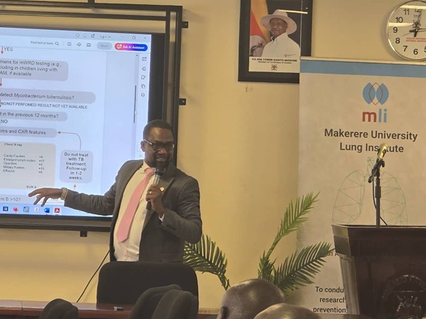 Man giving presentation. Standing, holding microphone and pointing at screen. 