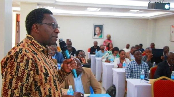 Man with glasses wearing a multicoloured shirt, holding a microphone, speaking to an audience